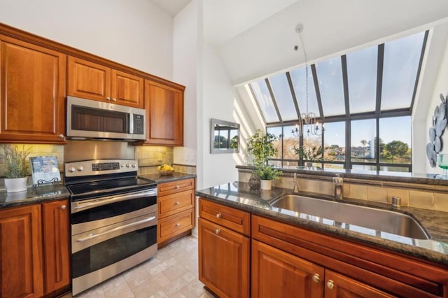 kitchen with a skylight, appliances with stainless steel finishes, dark stone countertops, and sink