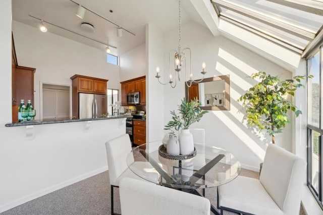 carpeted dining room featuring a skylight, a chandelier, track lighting, and a towering ceiling