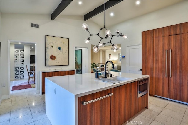 kitchen featuring stainless steel microwave, decorative light fixtures, lofted ceiling with beams, sink, and a kitchen island with sink