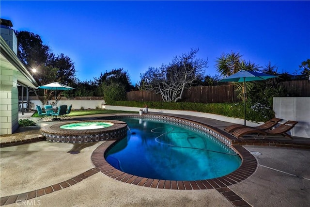 pool at dusk with an in ground hot tub and a patio