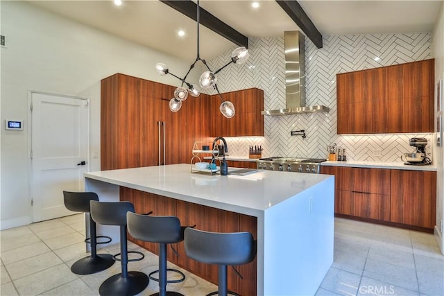 kitchen featuring range, a kitchen island with sink, wall chimney range hood, pendant lighting, and sink