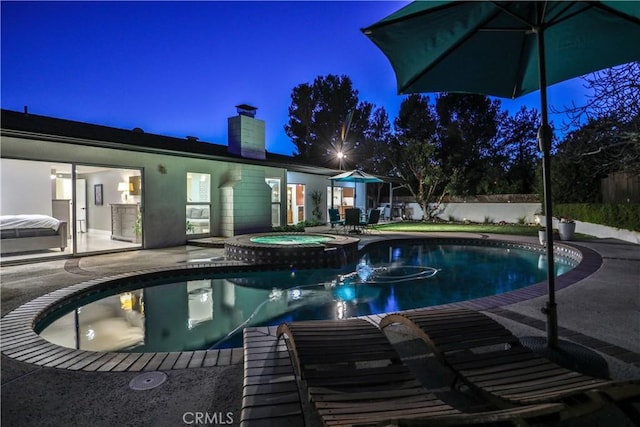 pool at night featuring an in ground hot tub and a patio