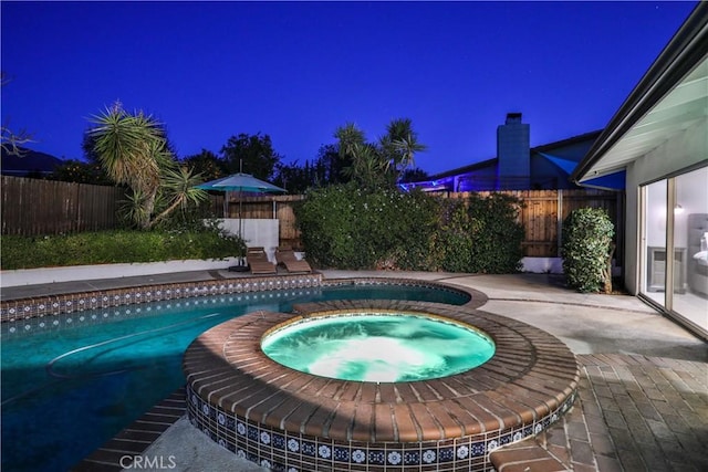 pool at twilight featuring an in ground hot tub and a patio area