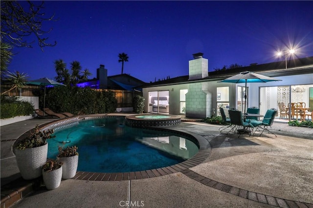 pool at twilight with a patio area and an in ground hot tub