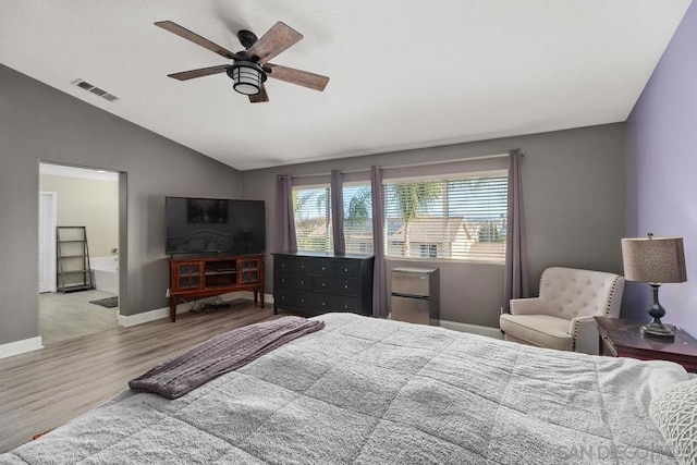 bedroom featuring ceiling fan, ensuite bath, vaulted ceiling, and light hardwood / wood-style flooring