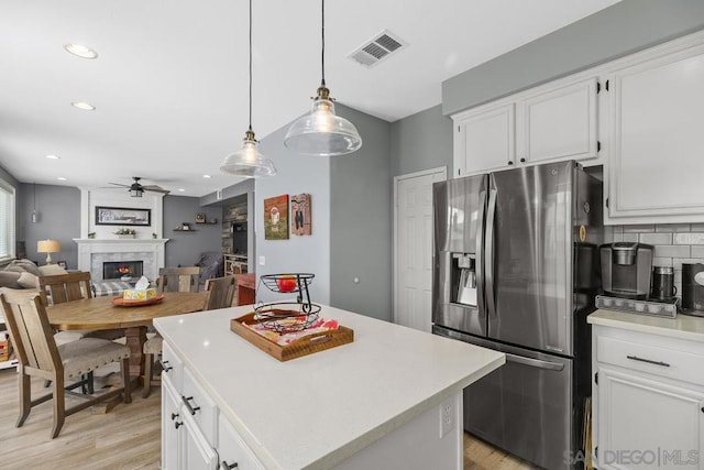 kitchen with ceiling fan, stainless steel fridge, white cabinetry, and a center island