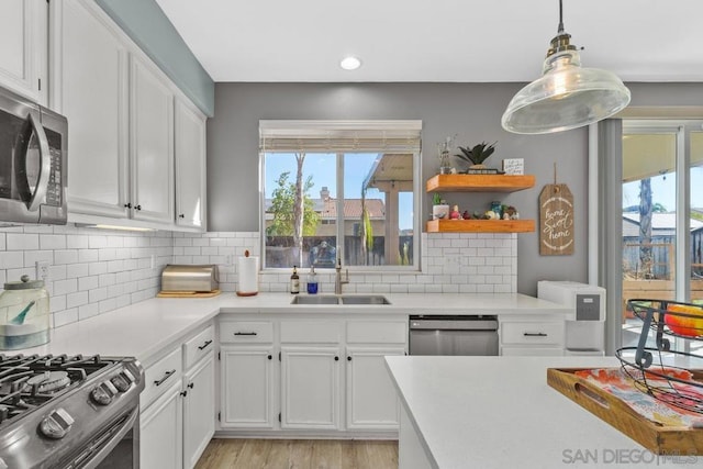 kitchen with pendant lighting, appliances with stainless steel finishes, white cabinetry, tasteful backsplash, and sink