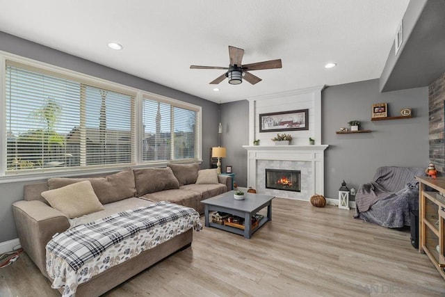 living room featuring a fireplace, ceiling fan, and light wood-type flooring