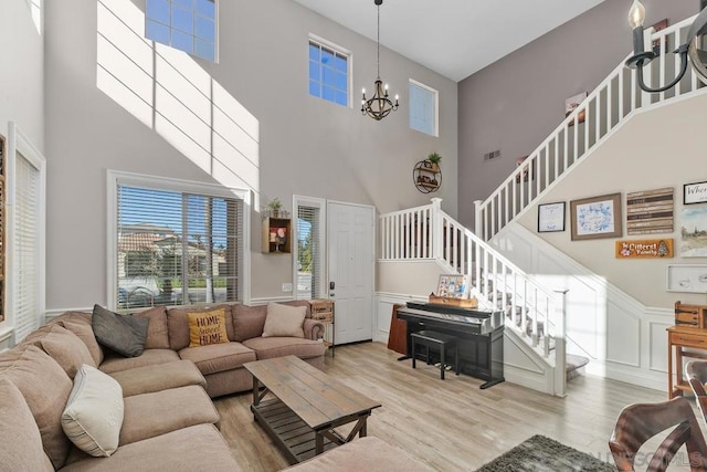 living room featuring light hardwood / wood-style floors, a towering ceiling, and a notable chandelier