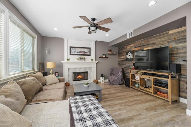 living room featuring ceiling fan, light hardwood / wood-style floors, a tiled fireplace, and wooden walls