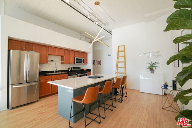 kitchen with a center island with sink, sink, hanging light fixtures, light wood-type flooring, and appliances with stainless steel finishes