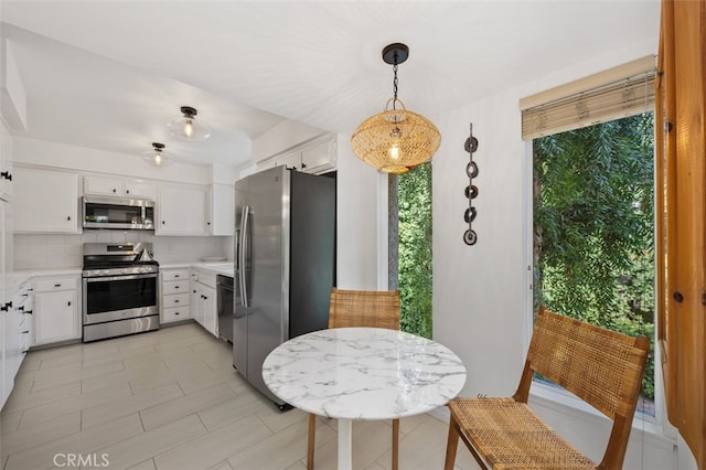 kitchen featuring white cabinetry, appliances with stainless steel finishes, backsplash, light tile patterned flooring, and pendant lighting