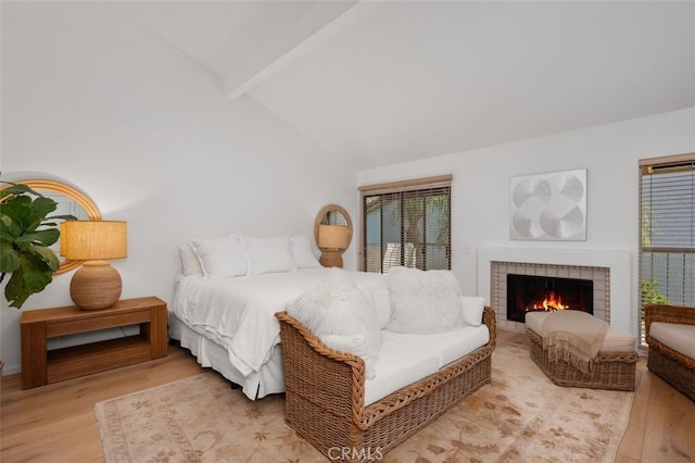 bedroom with light wood-type flooring, lofted ceiling with beams, and a fireplace