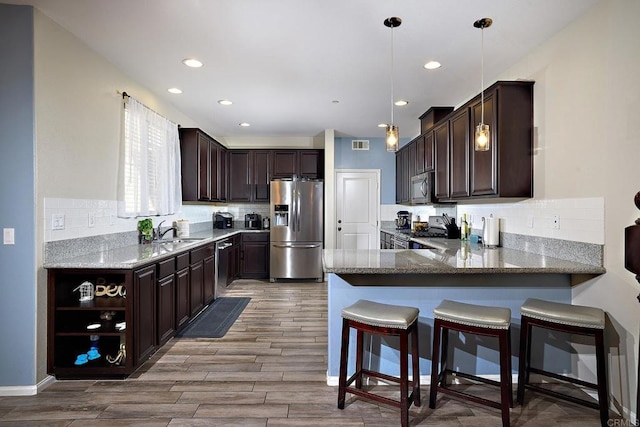 kitchen featuring stainless steel appliances, dark brown cabinetry, hanging light fixtures, and sink