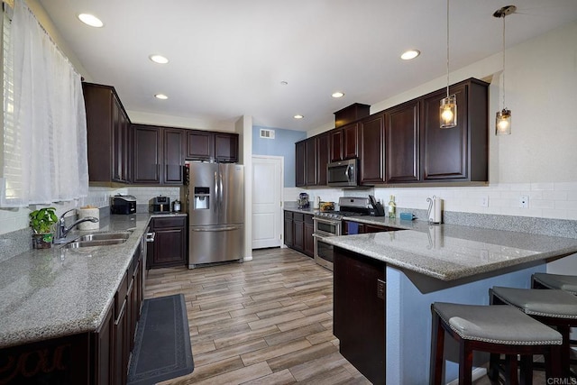 kitchen featuring kitchen peninsula, appliances with stainless steel finishes, decorative light fixtures, light stone counters, and sink