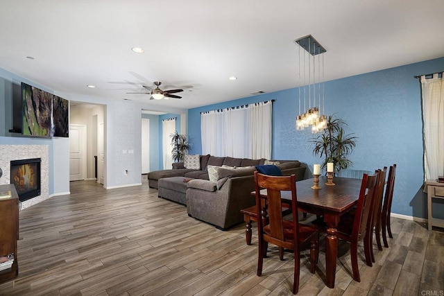 dining room featuring ceiling fan, wood-type flooring, and a tile fireplace