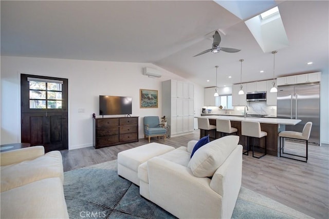 living room featuring sink, a wall mounted AC, light wood-type flooring, ceiling fan, and lofted ceiling with skylight