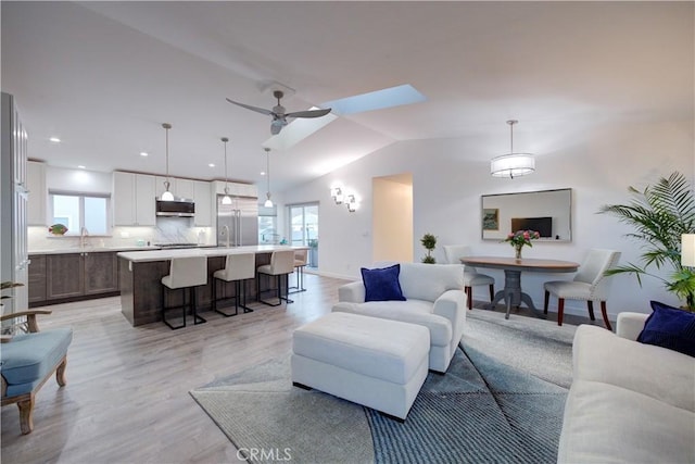 living room with ceiling fan, sink, vaulted ceiling, and light wood-type flooring