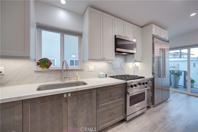 kitchen featuring white cabinetry, a healthy amount of sunlight, light stone countertops, high end appliances, and sink