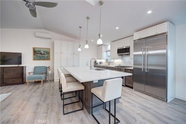 kitchen featuring white cabinetry, decorative backsplash, hanging light fixtures, high end appliances, and light stone counters