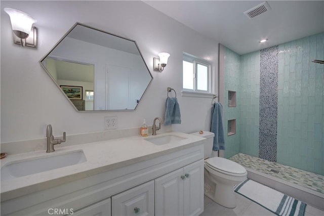 bathroom with toilet, vanity, tile patterned flooring, and tiled shower