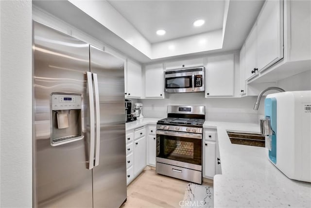 kitchen with light wood-type flooring, appliances with stainless steel finishes, white cabinetry, and sink