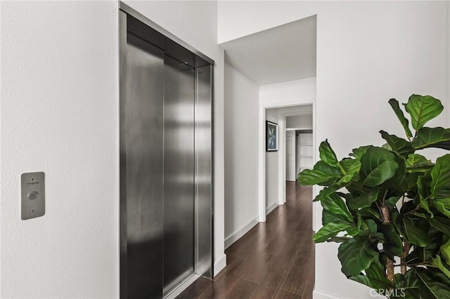 corridor featuring dark wood-style floors, elevator, and baseboards