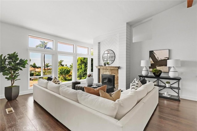 living room with visible vents, baseboards, dark wood-style flooring, and a glass covered fireplace