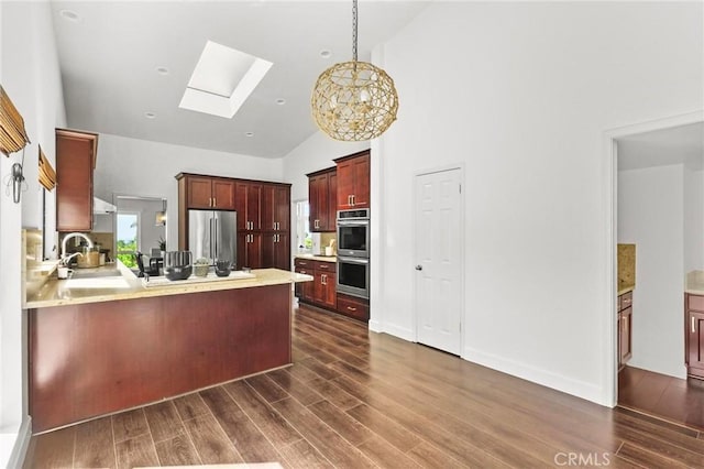 kitchen with a peninsula, a skylight, a sink, appliances with stainless steel finishes, and dark wood finished floors