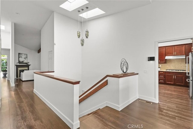 hall with dark wood-style flooring, baseboards, visible vents, and an upstairs landing