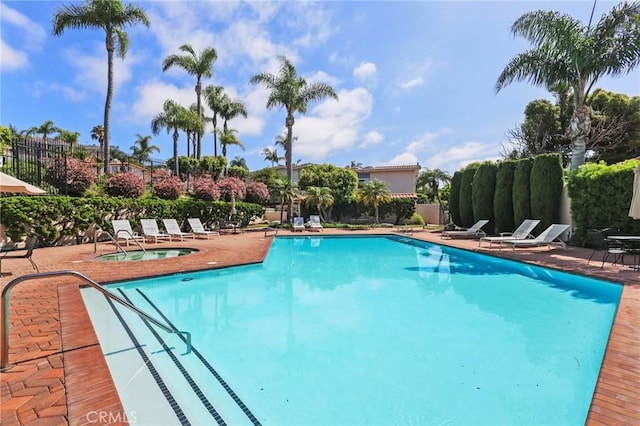 community pool featuring a patio area, fence, and a hot tub