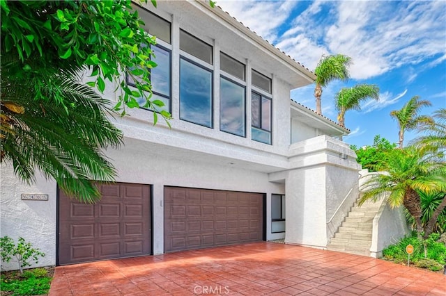 view of side of property featuring a garage, decorative driveway, stairway, and stucco siding