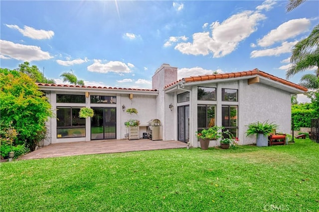 rear view of property with a chimney, a lawn, and stucco siding