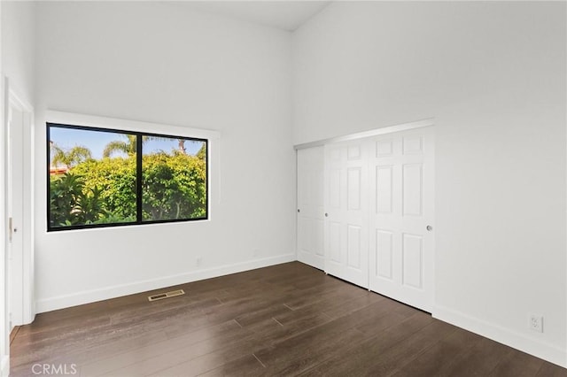 empty room with a towering ceiling, wood finished floors, visible vents, and baseboards