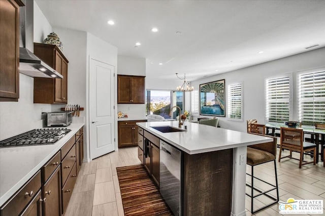 kitchen featuring wall chimney range hood, sink, an island with sink, a breakfast bar area, and stainless steel appliances