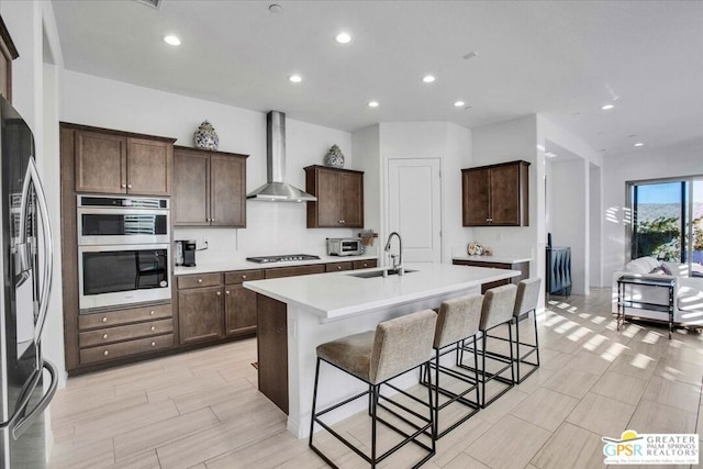 kitchen featuring wall chimney range hood, a center island with sink, sink, a breakfast bar area, and stainless steel appliances