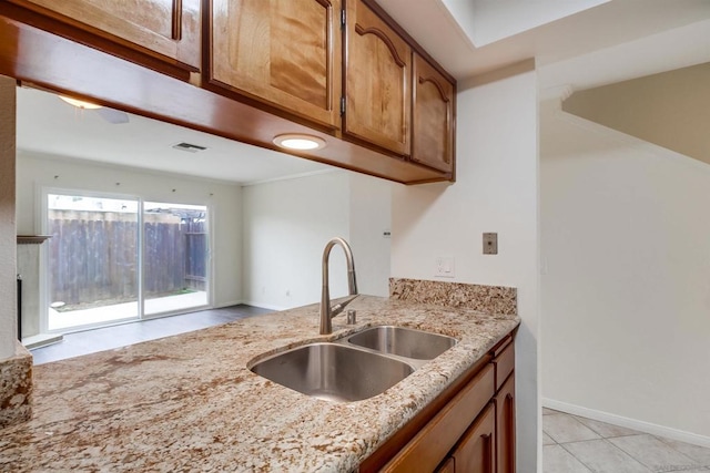 kitchen with light stone counters, sink, light tile patterned floors, and ornamental molding