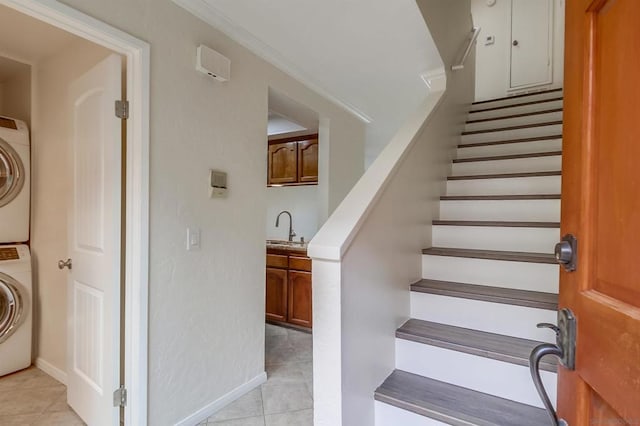 staircase with tile patterned flooring, stacked washer and dryer, sink, and ornamental molding