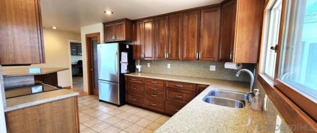 kitchen featuring light tile patterned floors, sink, backsplash, and stainless steel refrigerator