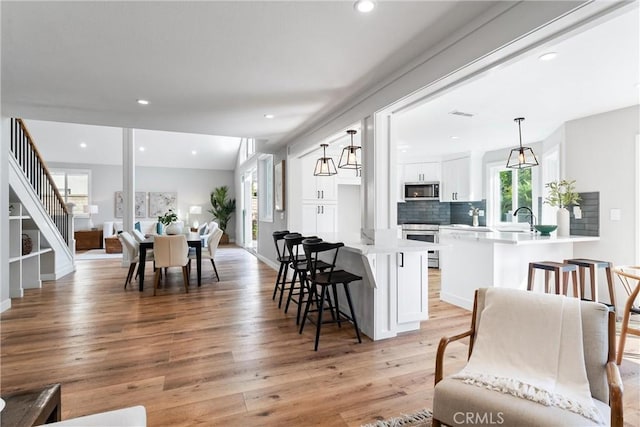 kitchen featuring white cabinets, stainless steel appliances, light hardwood / wood-style floors, hanging light fixtures, and kitchen peninsula