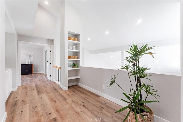 hall featuring vaulted ceiling, built in features, and light hardwood / wood-style flooring