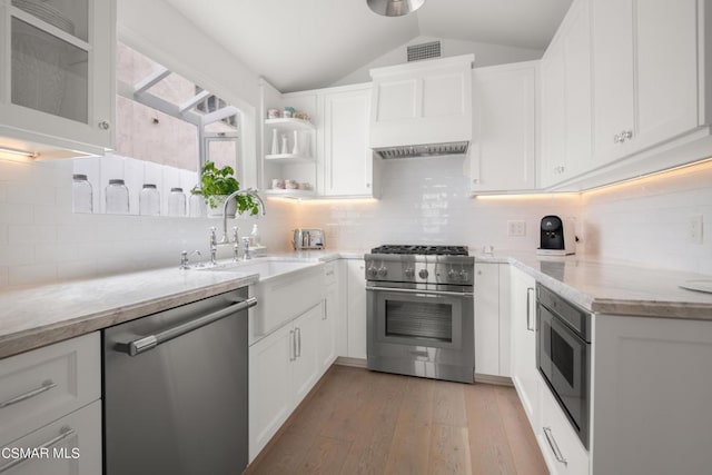 kitchen featuring vaulted ceiling, appliances with stainless steel finishes, white cabinetry, light stone counters, and light hardwood / wood-style flooring