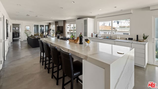 kitchen featuring a center island, white cabinetry, sink, light stone counters, and a breakfast bar area