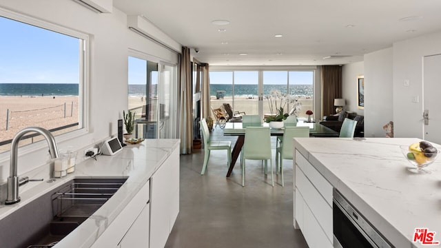 kitchen featuring white cabinetry, a water view, a beach view, and sink