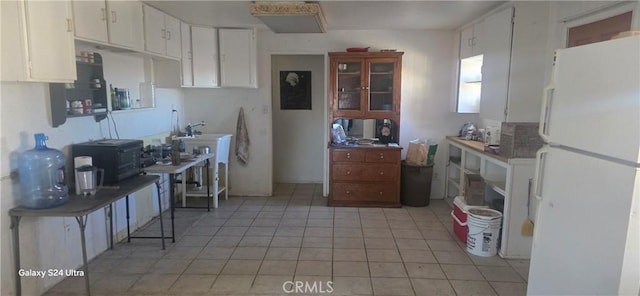 kitchen with white fridge, light tile patterned flooring, and white cabinets