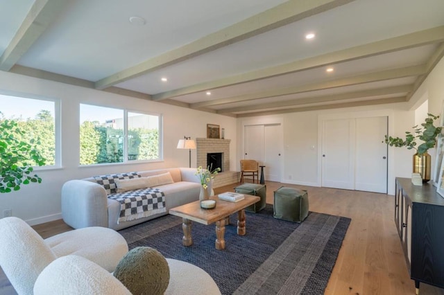 living room featuring a brick fireplace, beam ceiling, and light hardwood / wood-style flooring