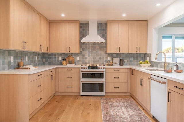 kitchen featuring light brown cabinetry, sink, backsplash, wall chimney range hood, and white appliances