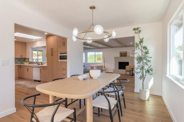 dining area featuring a brick fireplace, a healthy amount of sunlight, a notable chandelier, and light hardwood / wood-style floors