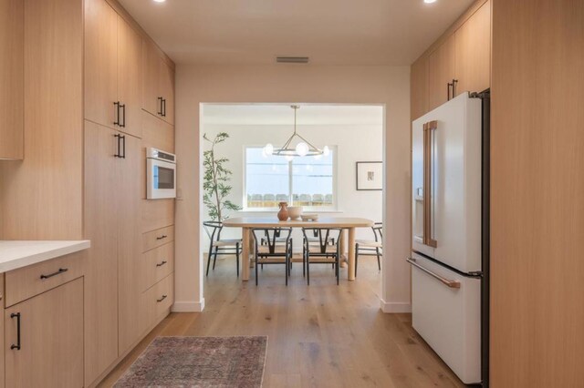 kitchen with high end fridge, light brown cabinetry, decorative light fixtures, a chandelier, and light hardwood / wood-style floors