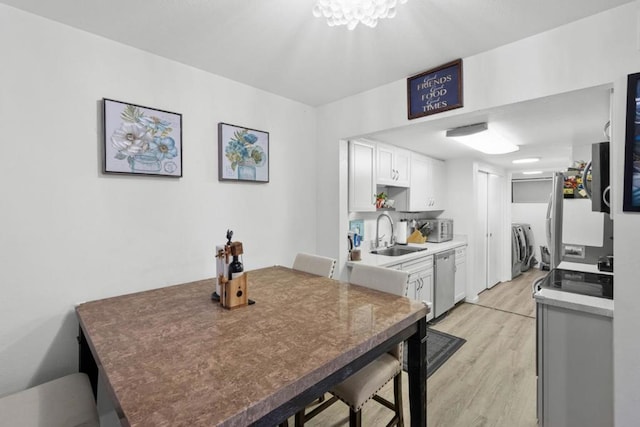 kitchen with washer and dryer, appliances with stainless steel finishes, white cabinetry, sink, and light hardwood / wood-style flooring